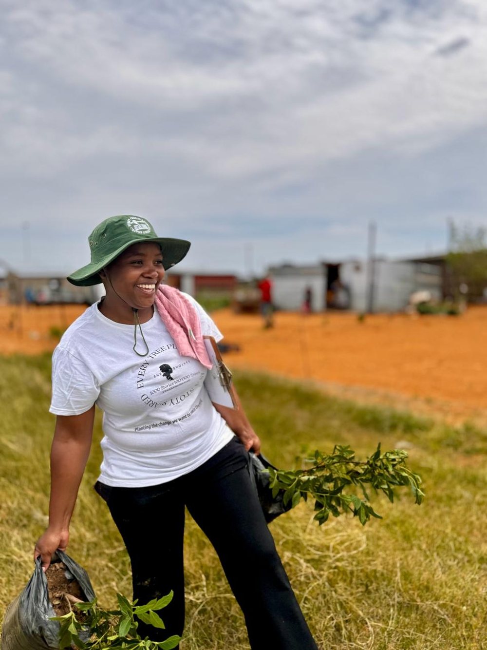 A Change Maker in a She Evolves shirt carrying saplings across the field, laughing
