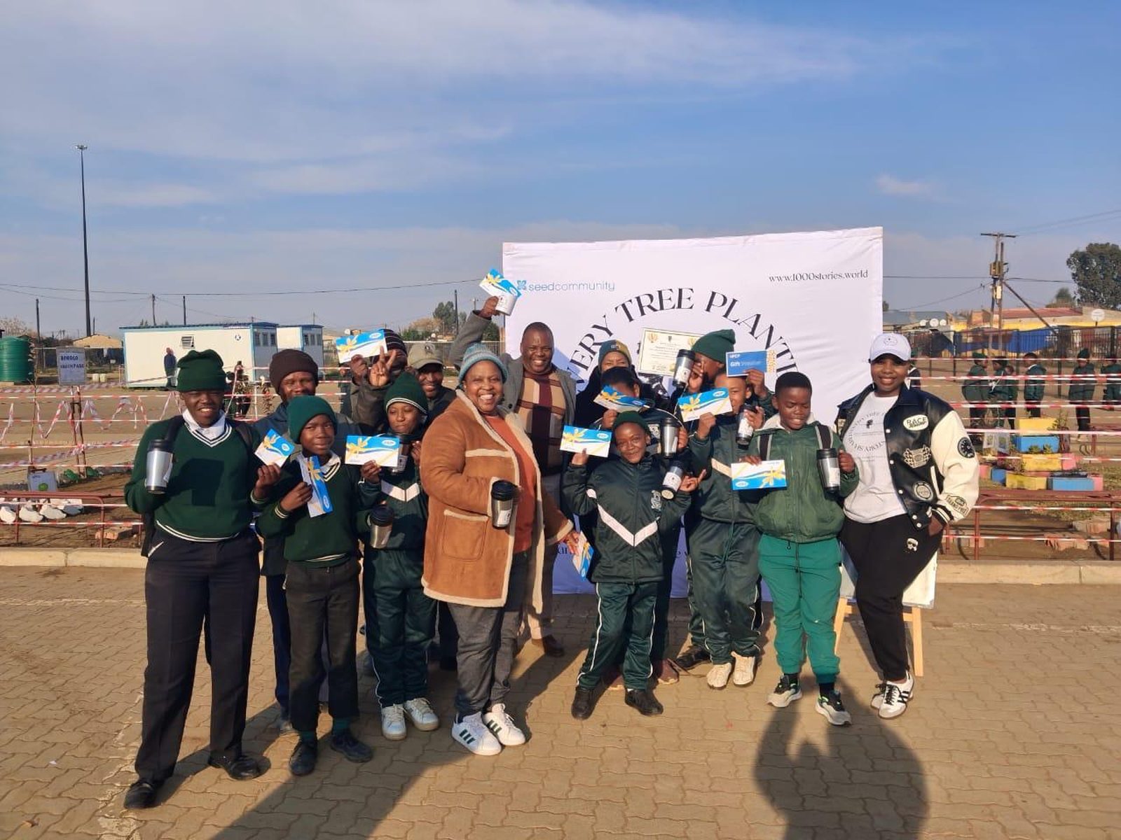Learners and Change Makers holding certificates and flasks in front of the 1000 Stories banner after a planting day